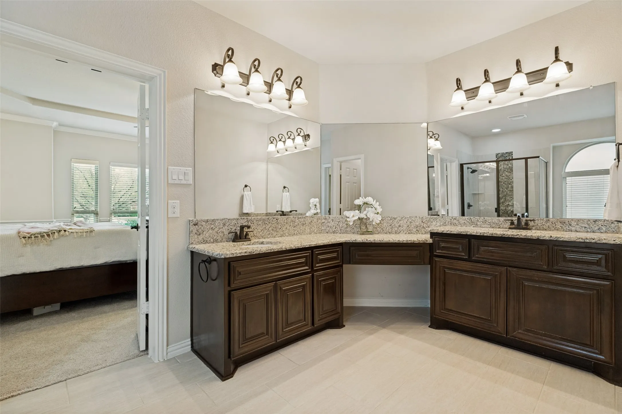 Dual vanity featuring granite countertops, undermount sinks, dark wood cabinetry, and extensive wall-mounted mirrors
