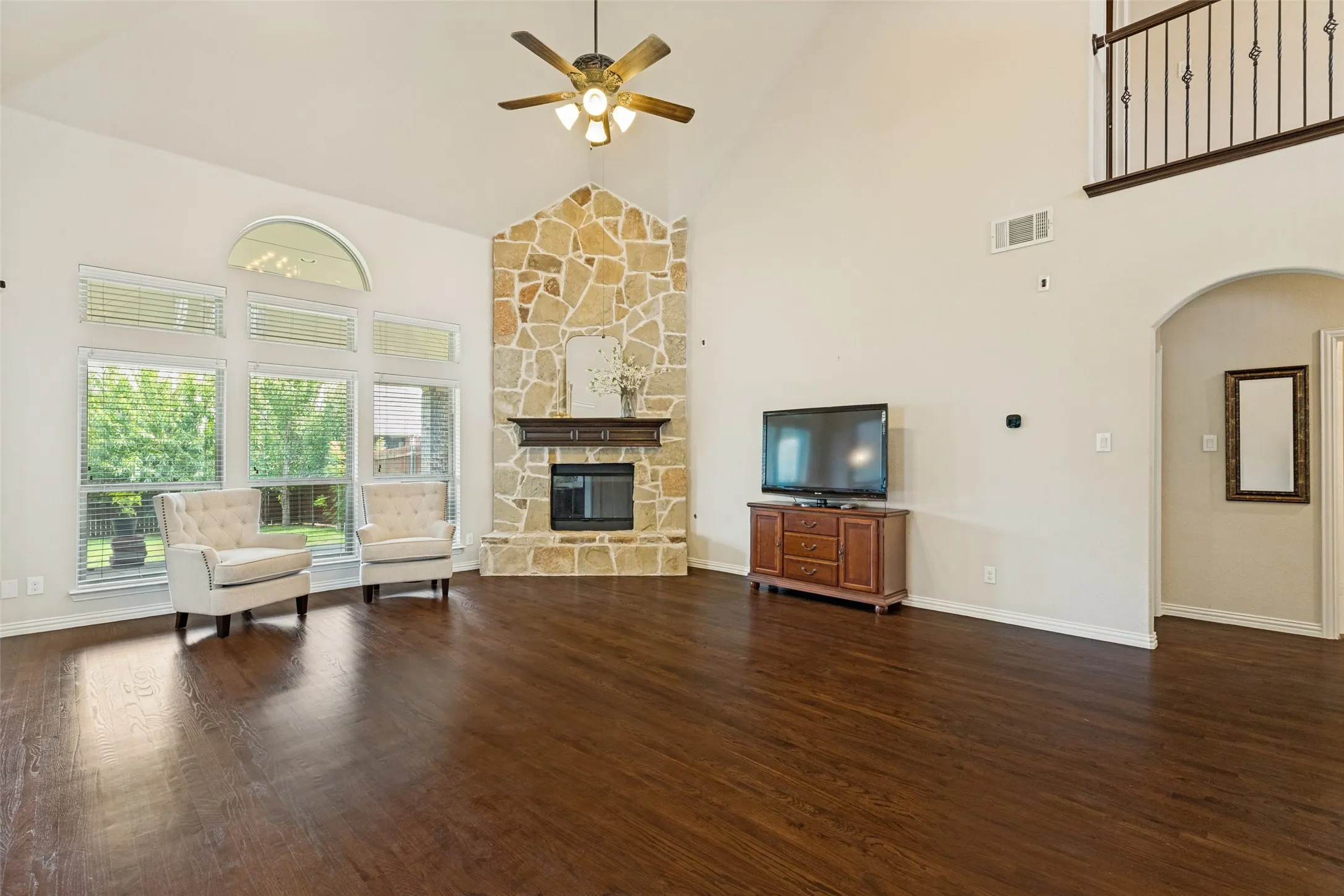 Living room featuring a vaulted ceiling with a ceiling fan, a stone-faced fireplace with a wood mantle, wood-finish flooring, and expansive windows