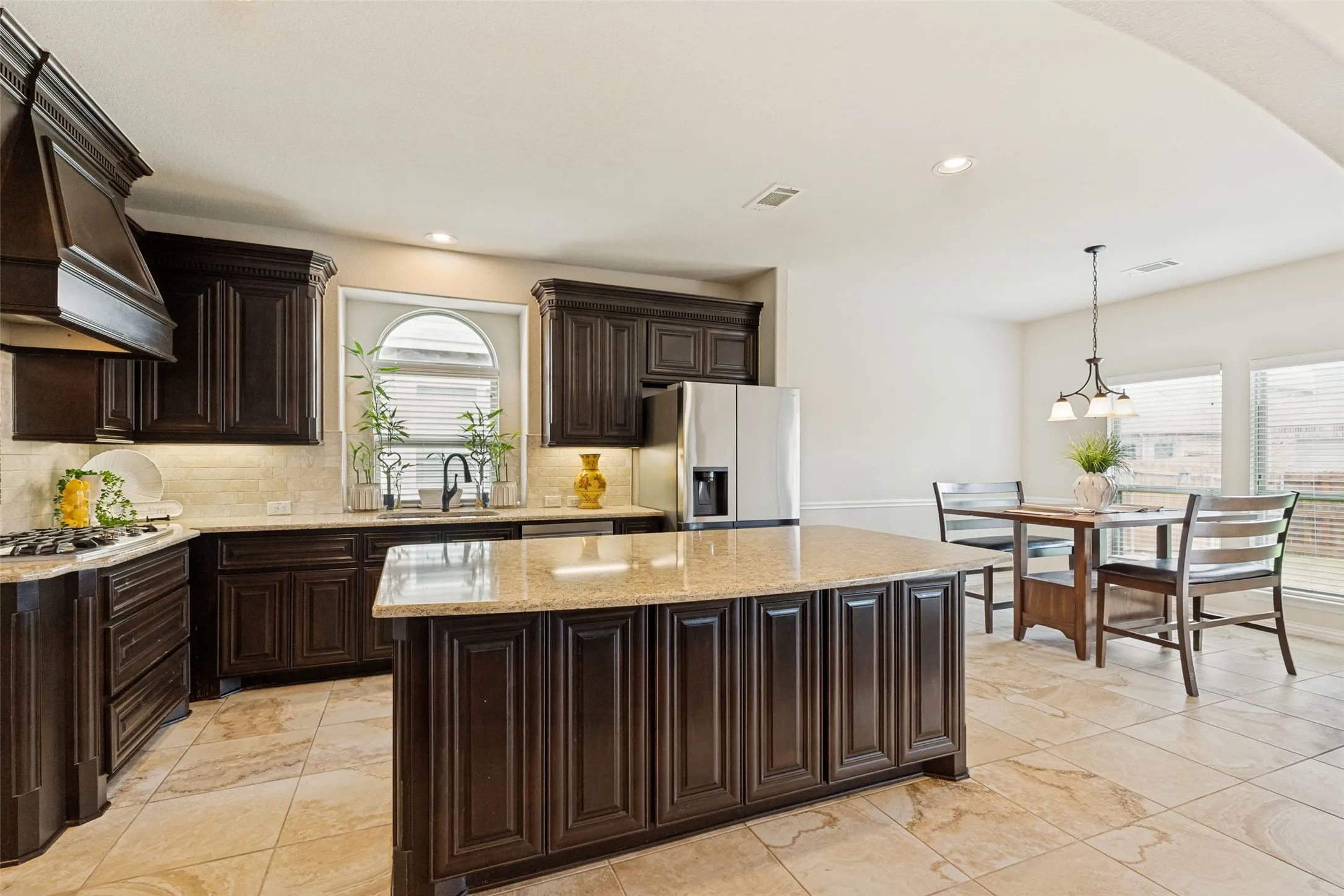 Kitchen featuring dark wood cabinetry, light-toned countertops, a central island with additional storage, stainless steel appliances, and tile flooring
