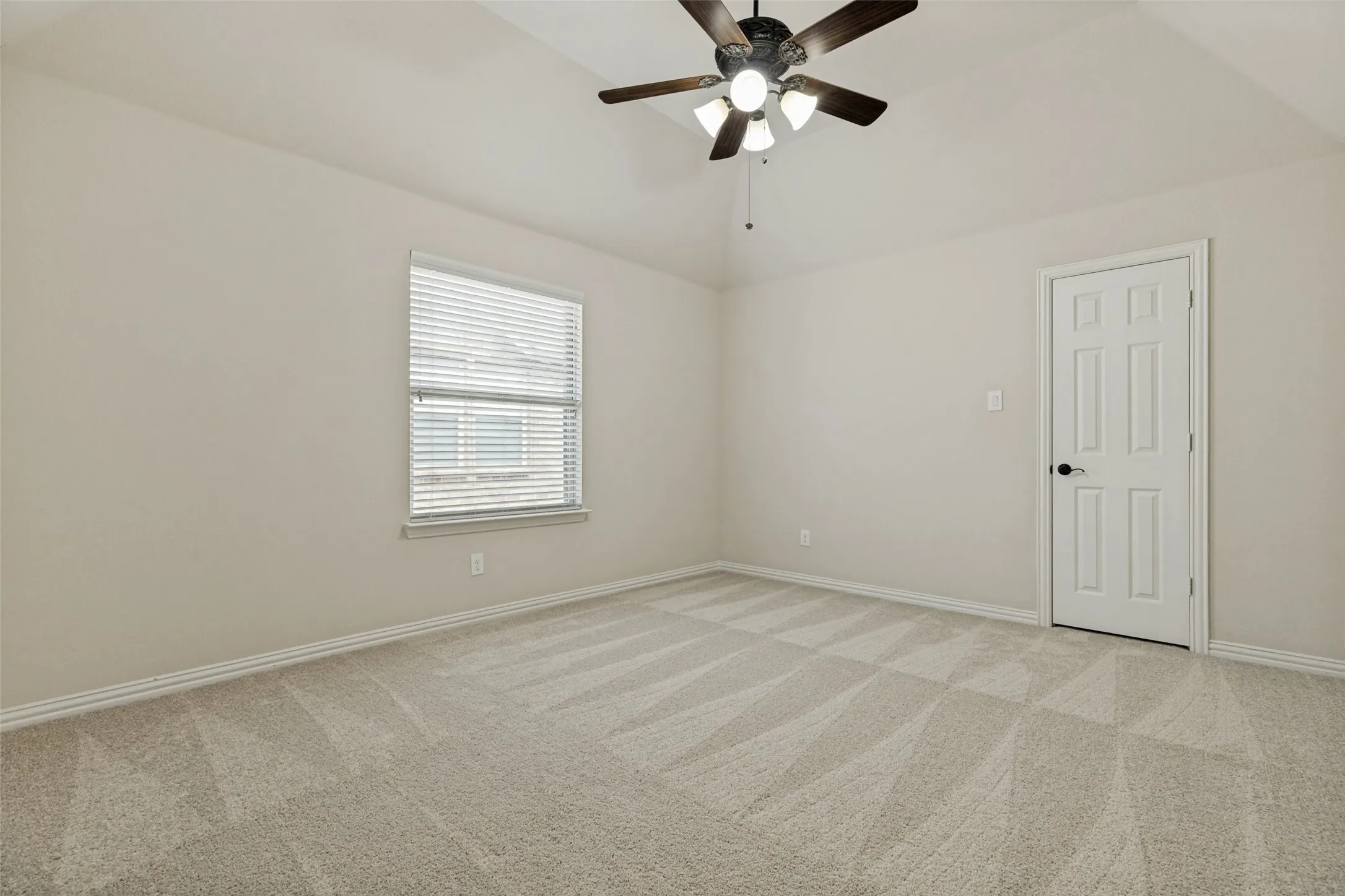 Spacious room featuring vaulted ceilings, light-toned carpeting, and a ceiling fan with integrated lighting
