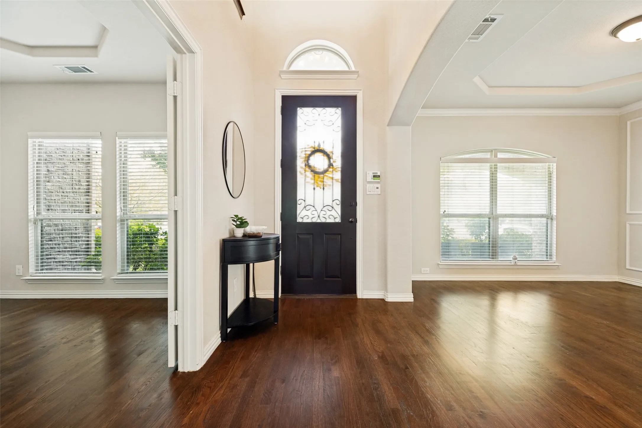 Entryway featuring wood-finish flooring, a dark wood door with decorative glass and an arched transom, and recessed ceiling details