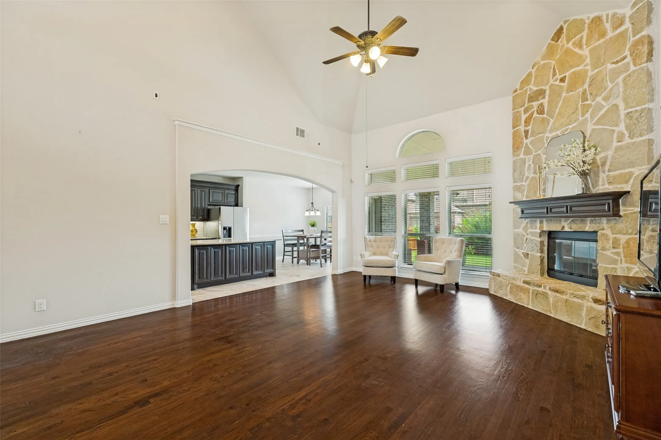 Spacious living area featuring high vaulted ceilings, wood-finish flooring, and a stone-clad fireplace with a dark wood mantel