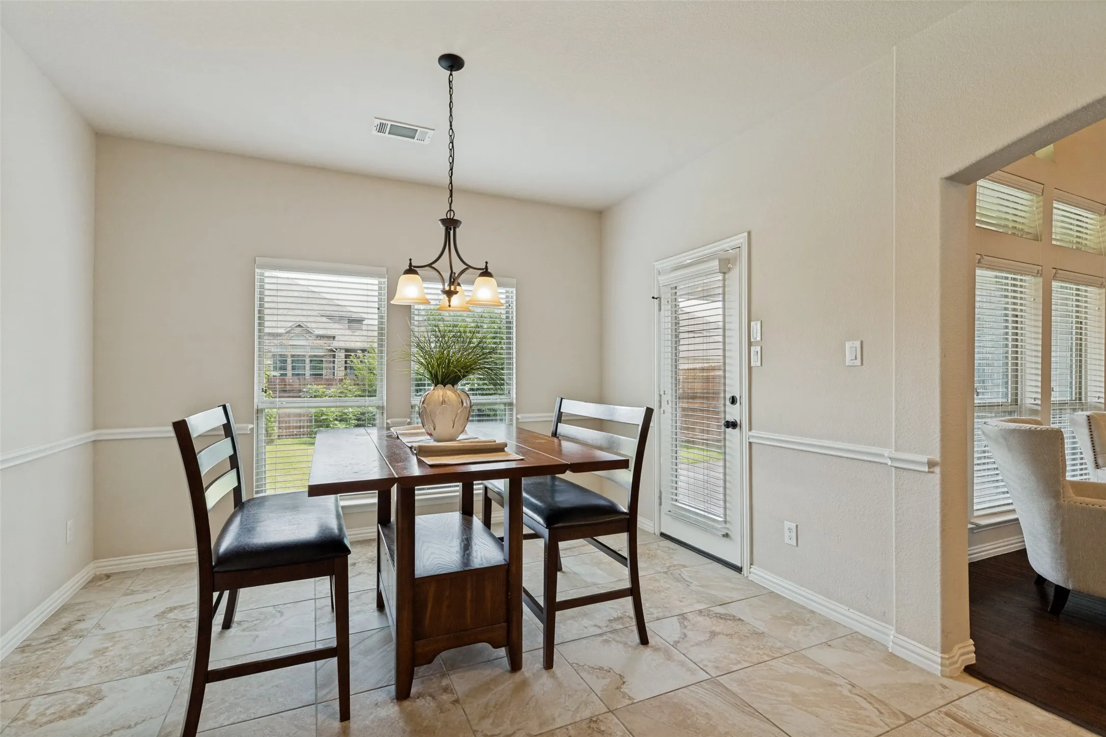 Dining area featuring tile flooring, wainscoting, an overhead chandelier, and two windows with blinds