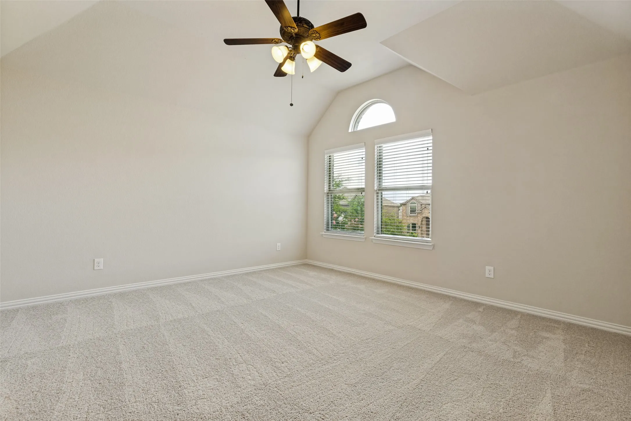 Spacious room featuring vaulted ceilings, light-colored carpeting, and a ceiling fan with integrated lighting