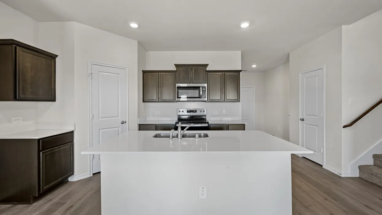 Kitchen featuring a large central island with an integrated double basin sink, dark wood-finish cabinetry, light-toned countertops, stainless steel appliances, and recessed lighting