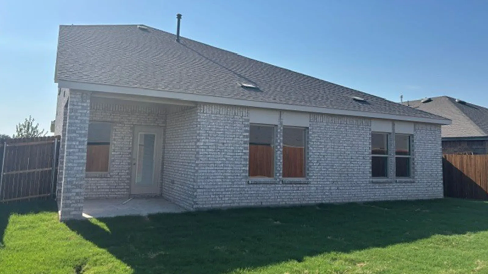 Brick exterior with covered patio, concrete slab, and wood privacy fencing
