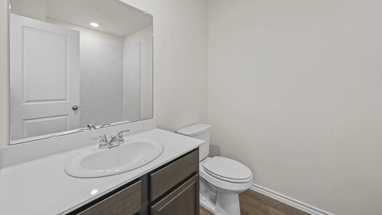 Bathroom vanity featuring a white oval sink with chrome faucet, light-toned countertop, and wood-finish cabinetry