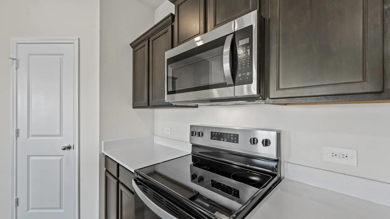 Kitchen featuring dark-stained cabinetry, stainless steel microwave, stainless steel electric range, and light-toned countertops