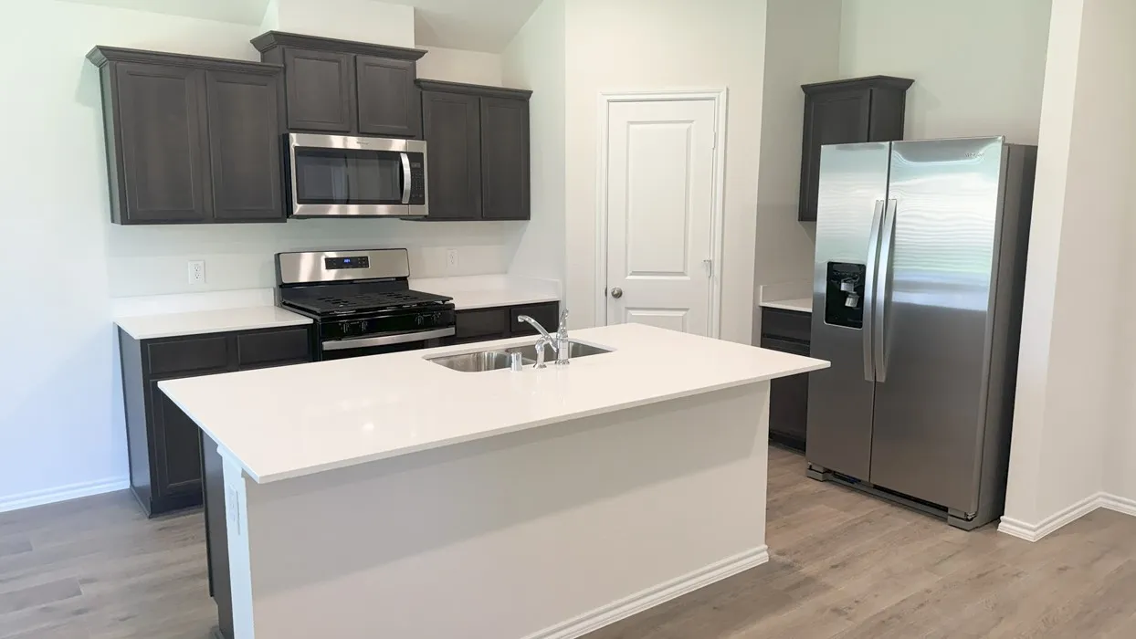 Kitchen featuring a central island with an integrated sink, dark wood-finish cabinetry, stainless steel appliances, white countertops, and wood-finish flooring