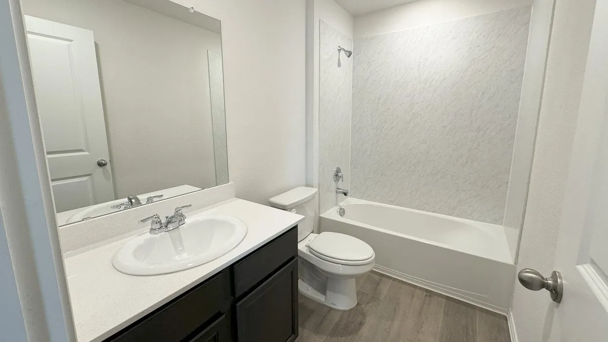 Bathroom featuring a white bathtub with a textured surround, a dark wood-finish vanity with a white countertop and integrated sink, and wood-finish flooring