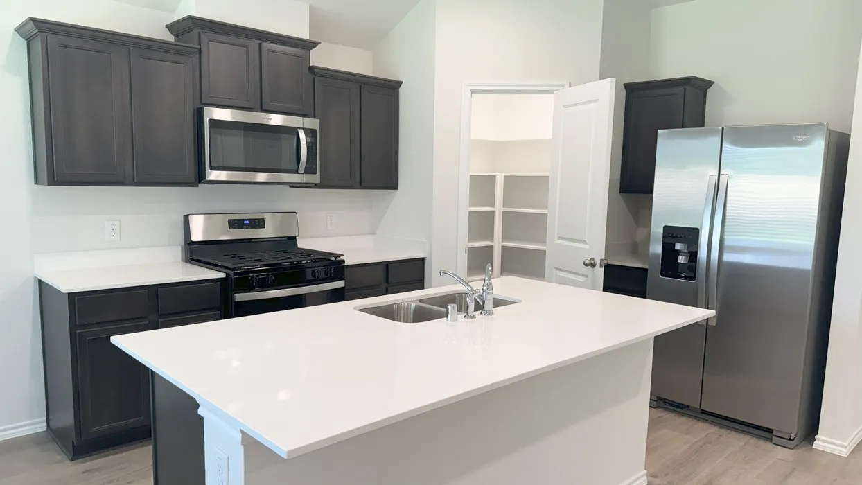 Modern kitchen featuring dark wood-finish cabinetry, stainless steel appliances, white countertops, and a central island with a double sink