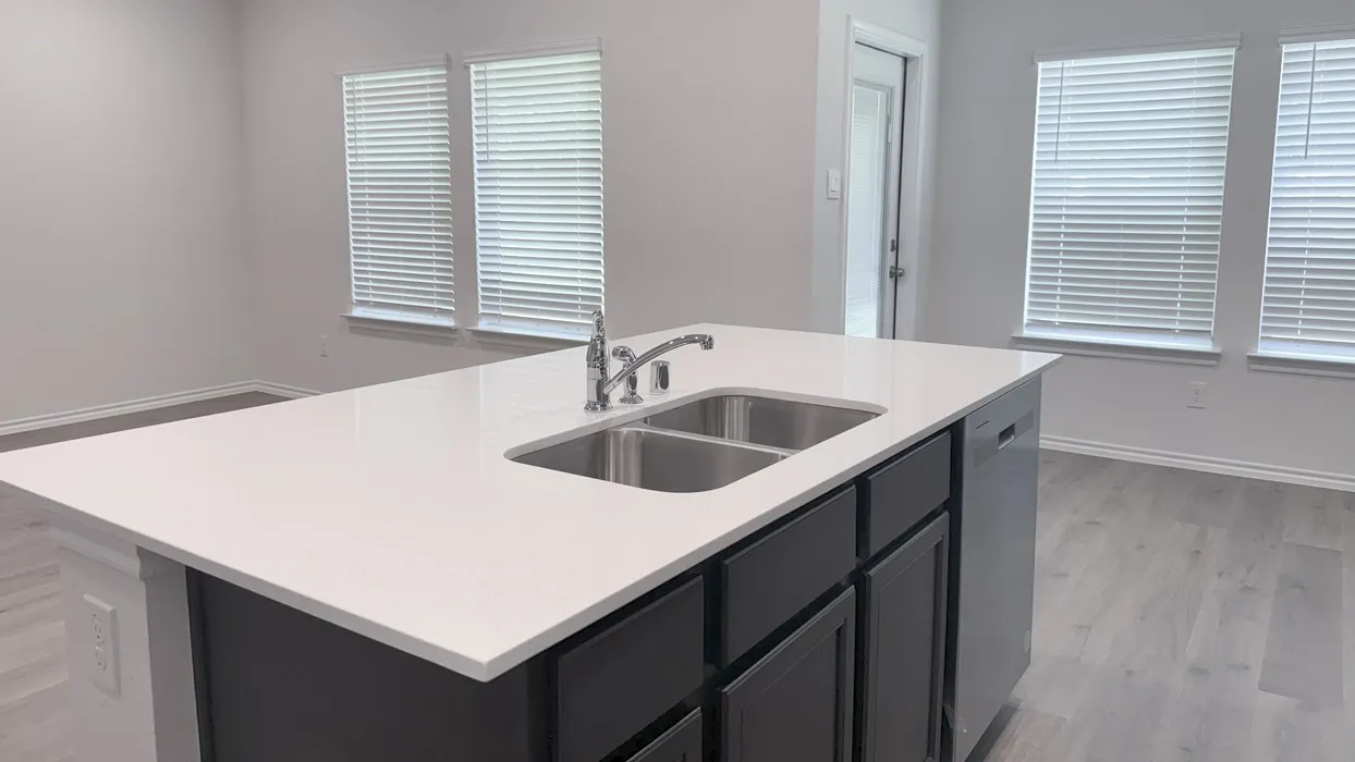Kitchen island featuring a white countertop with an undermount double-basin stainless steel sink and a chrome faucet