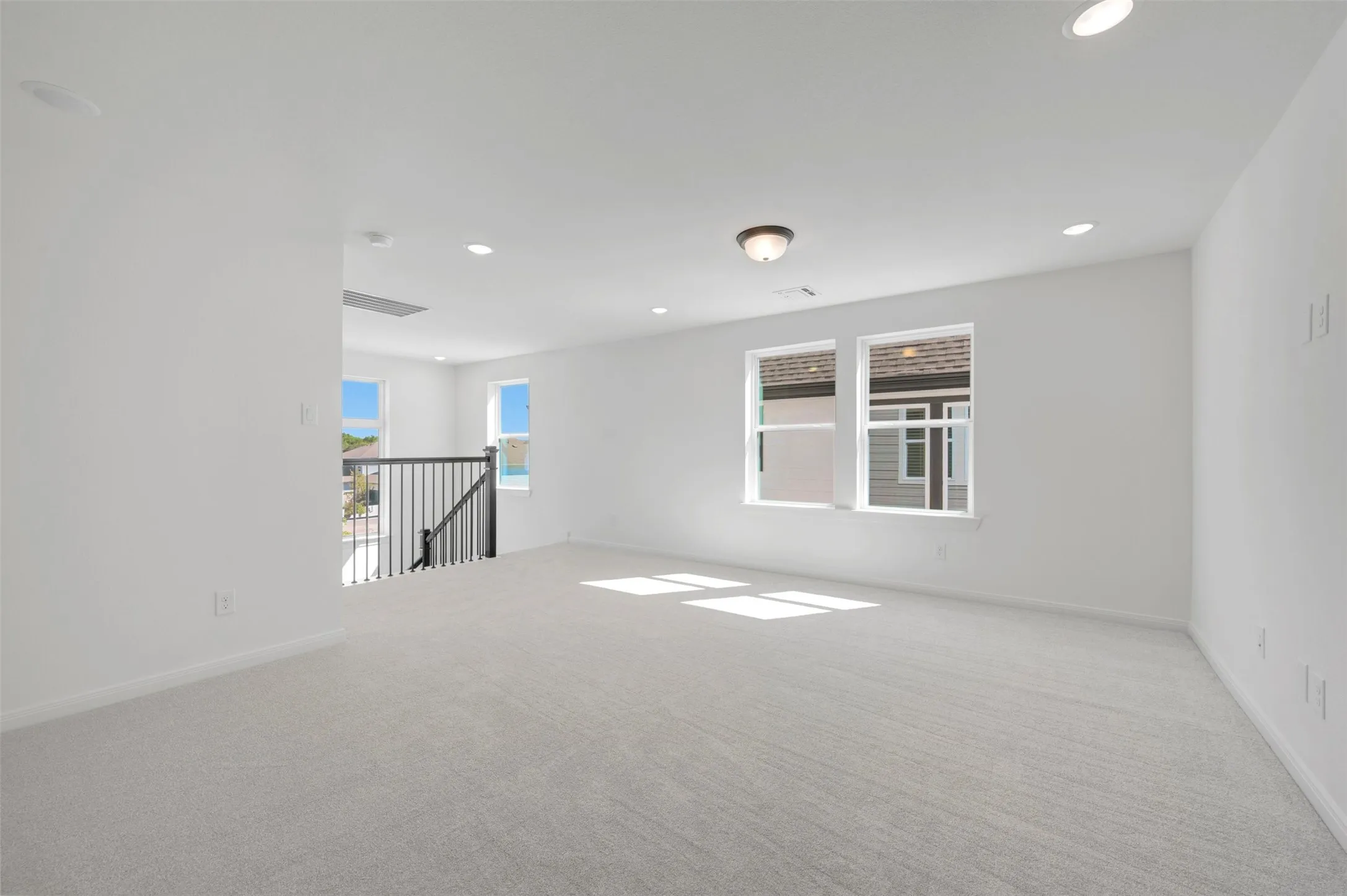 Open loft space featuring light-toned carpeting, recessed lighting, and multiple windows