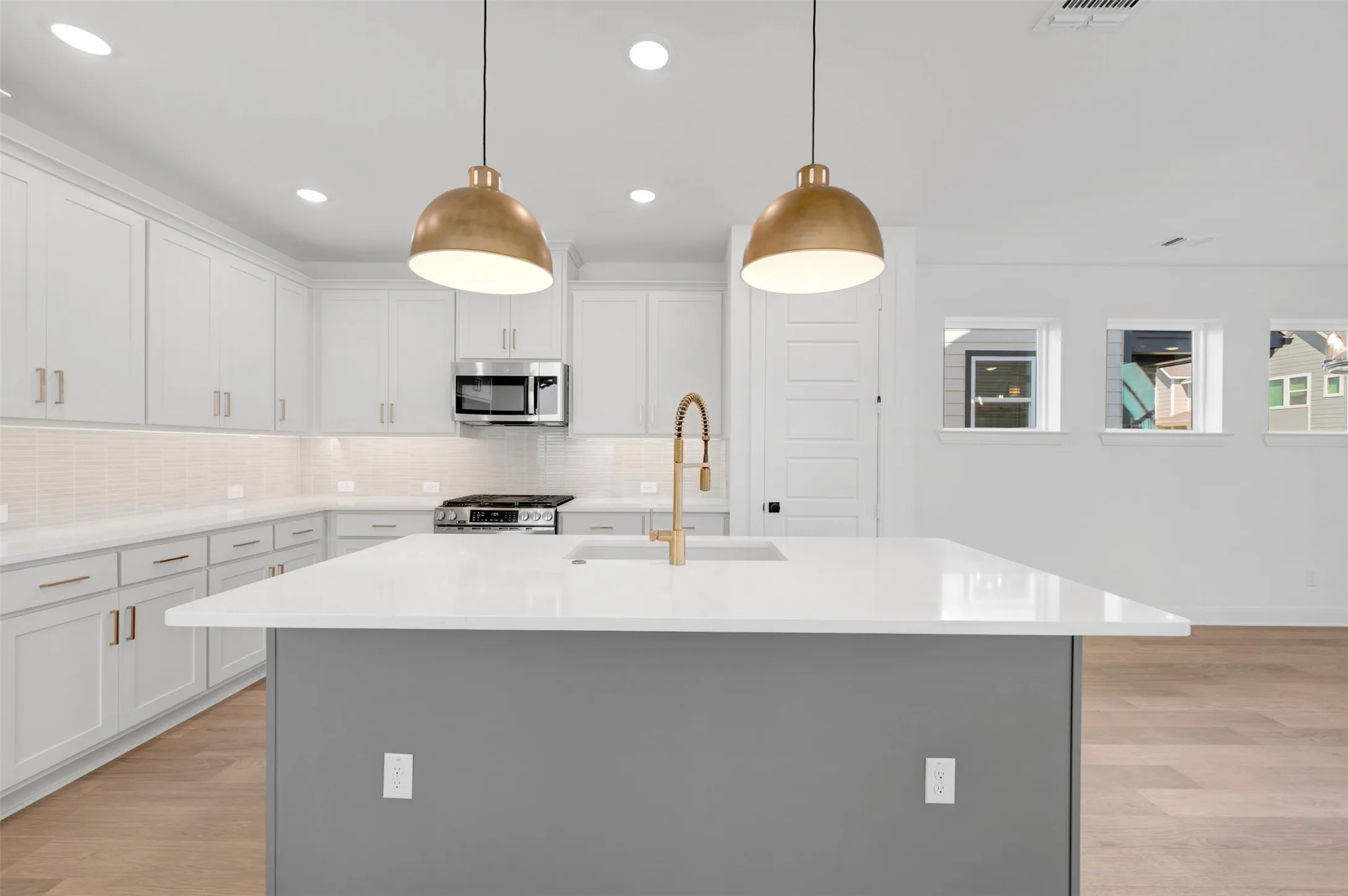 Kitchen featuring a large island with a light-toned countertop, white cabinetry with gold-toned hardware, a stainless steel gas range, and wood-finish flooring