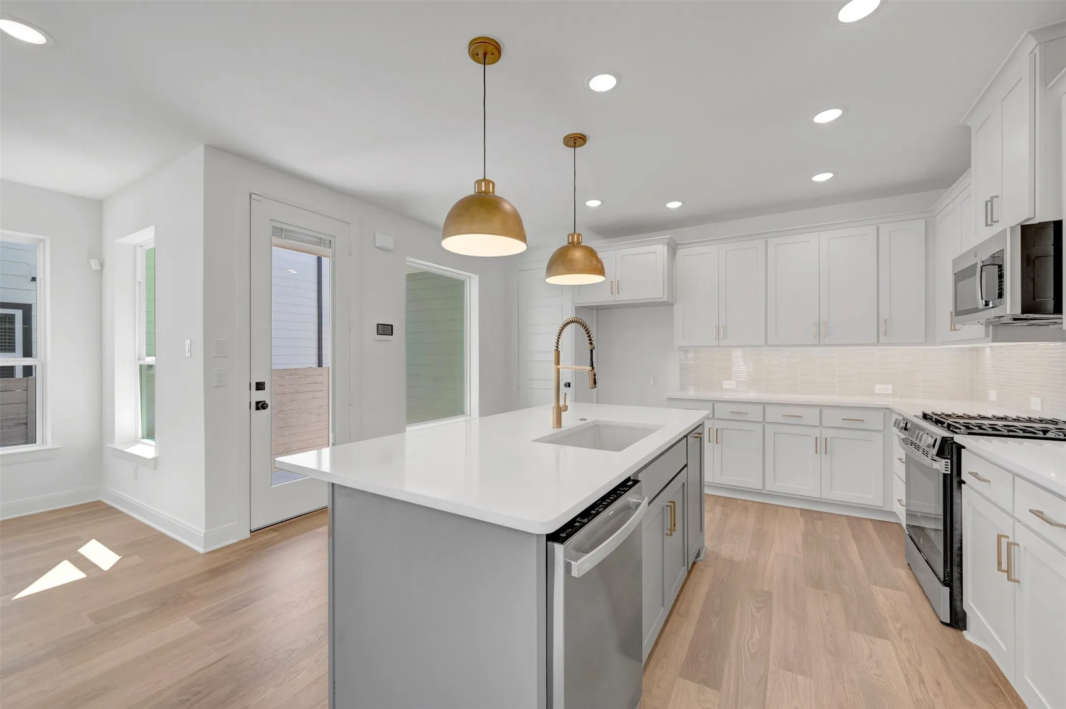 Kitchen featuring an island with a built-in sink, stainless steel appliances, white cabinetry, recessed lighting, and wood-finish flooring