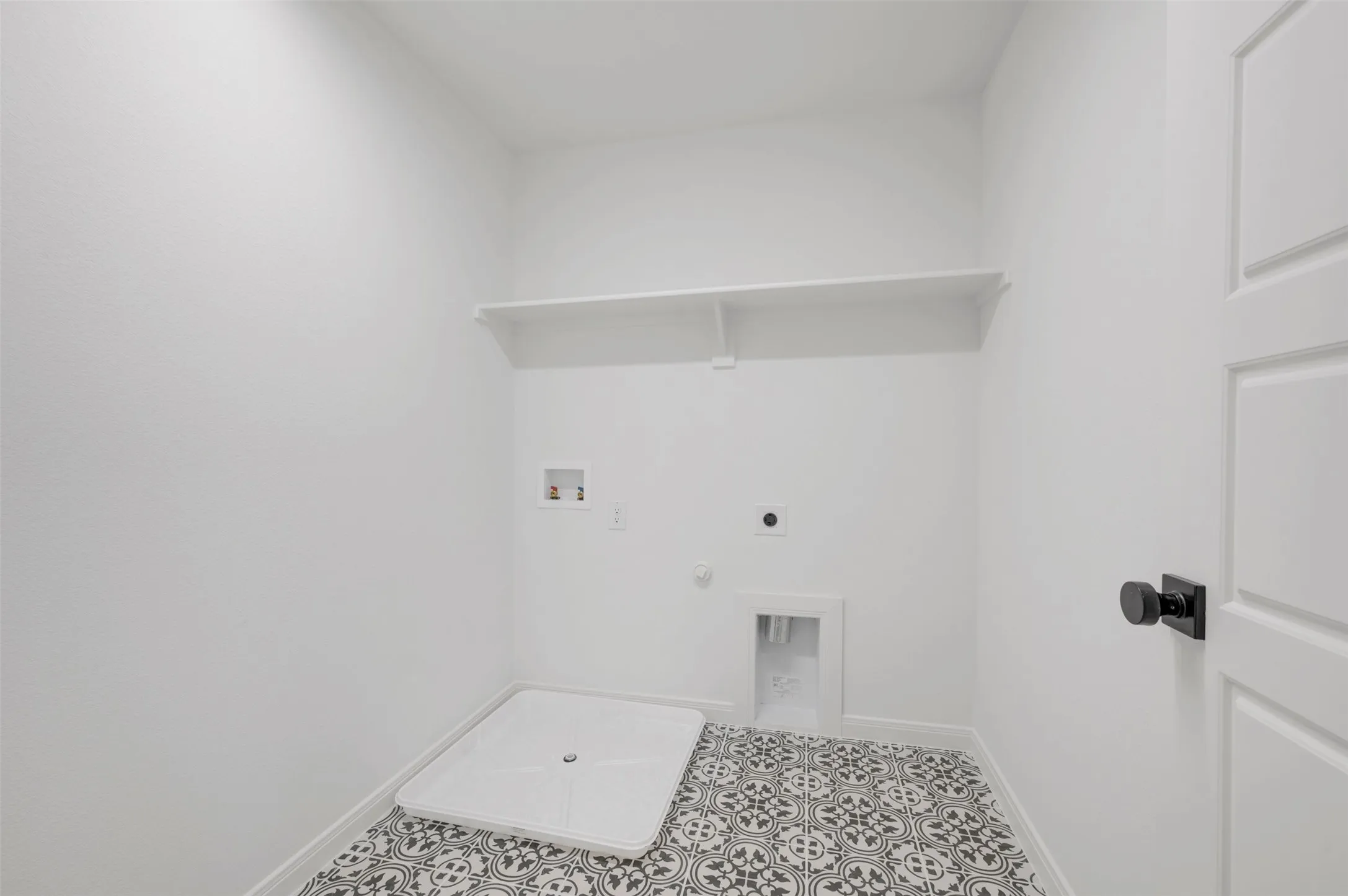 Utility room featuring patterned tile flooring, built-in shelving, and a white paneled door with matte black hardware