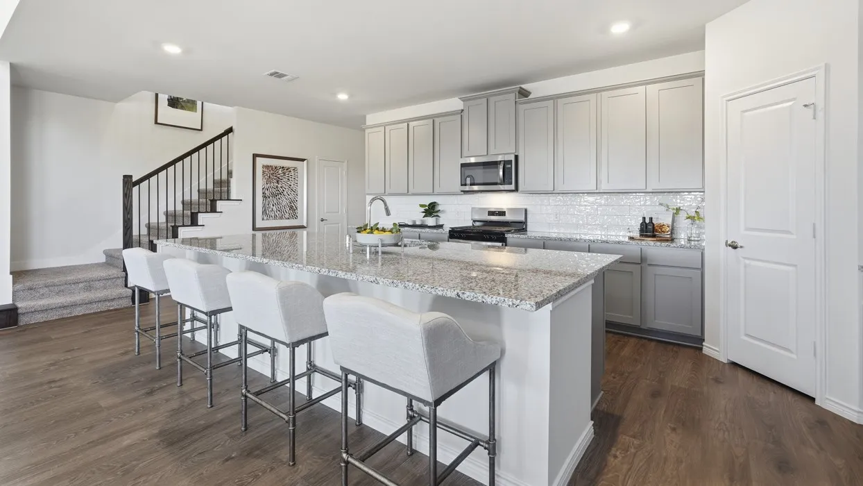 Open-concept kitchen featuring an oversized island with ample seating, light-toned cabinetry, stainless steel appliances, a subway tile backsplash, and wood-finish flooring