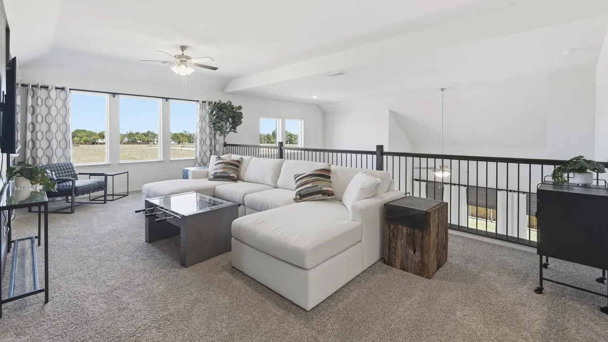 Spacious upper-level loft featuring carpet flooring, multiple windows, a ceiling fan, and a black iron railing overlooking the lower level