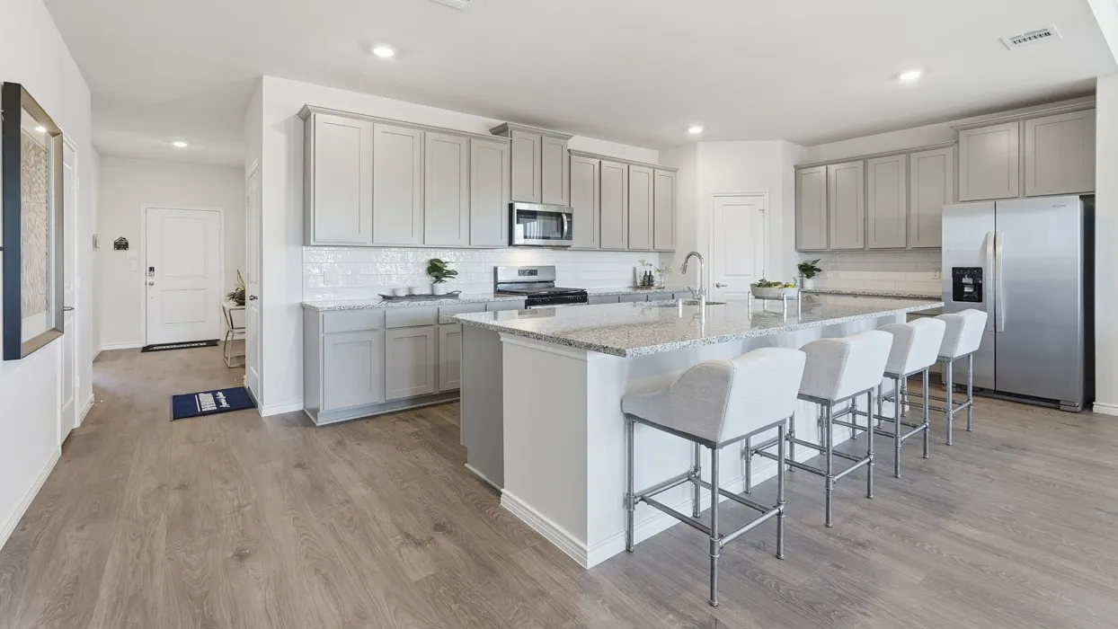 Open-concept kitchen featuring an oversized island with seating, stainless steel appliances, light gray cabinetry, and wood-finish flooring