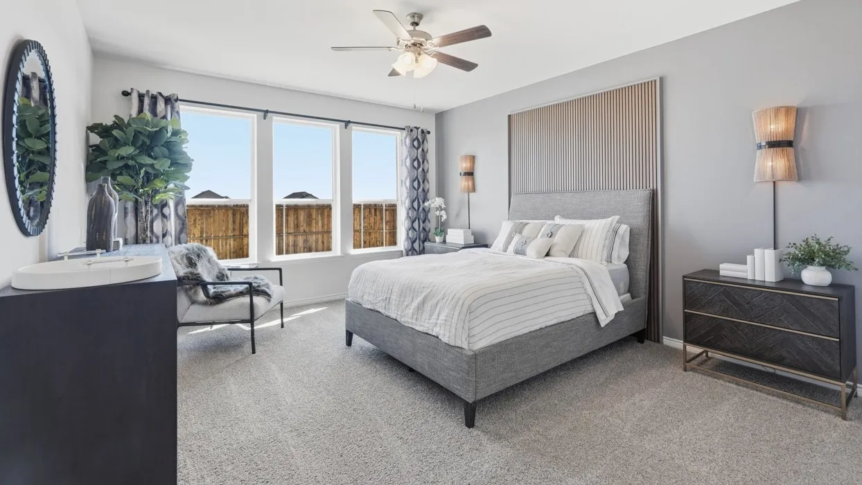 Carpeted interior space featuring a ceiling fan with integrated lighting, three large windows, and a built-in wall panel accenting the bed frame