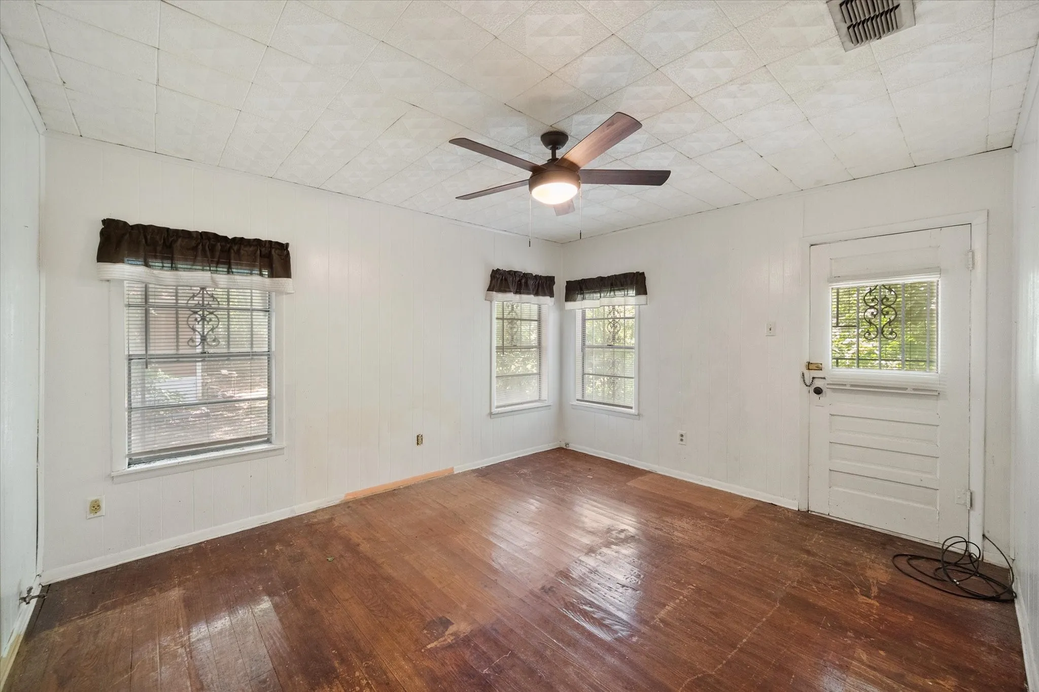 This spacious bedroom features hardwood flooring, a ceiling fan, multiple windows, and direct exterior access.