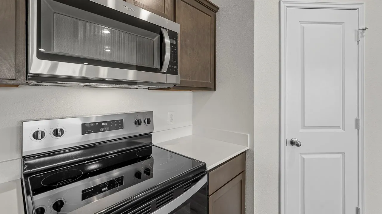 Kitchen featuring stainless steel appliances, dark wood-finish cabinetry, light-toned countertops, and a white paneled door