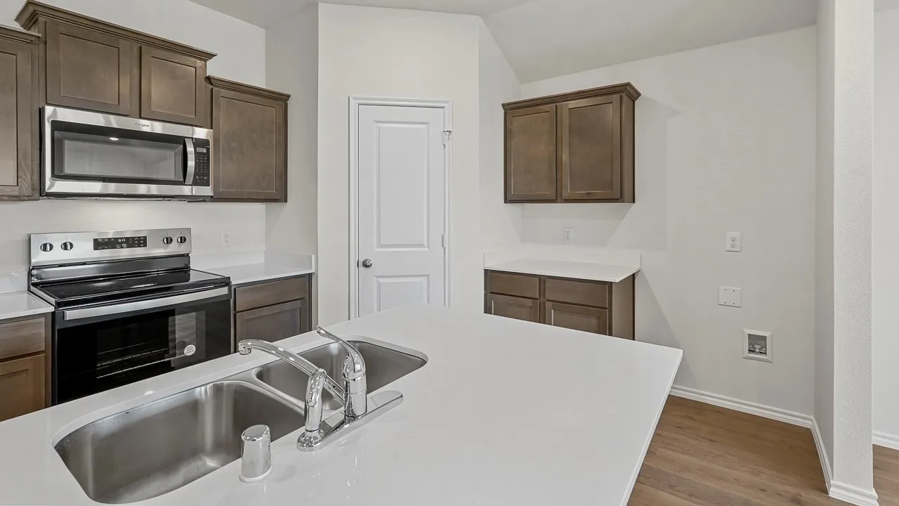 Kitchen featuring a large island with dual stainless steel sinks, dark wood cabinetry, white countertops, stainless steel microwave, and stainless steel electric range