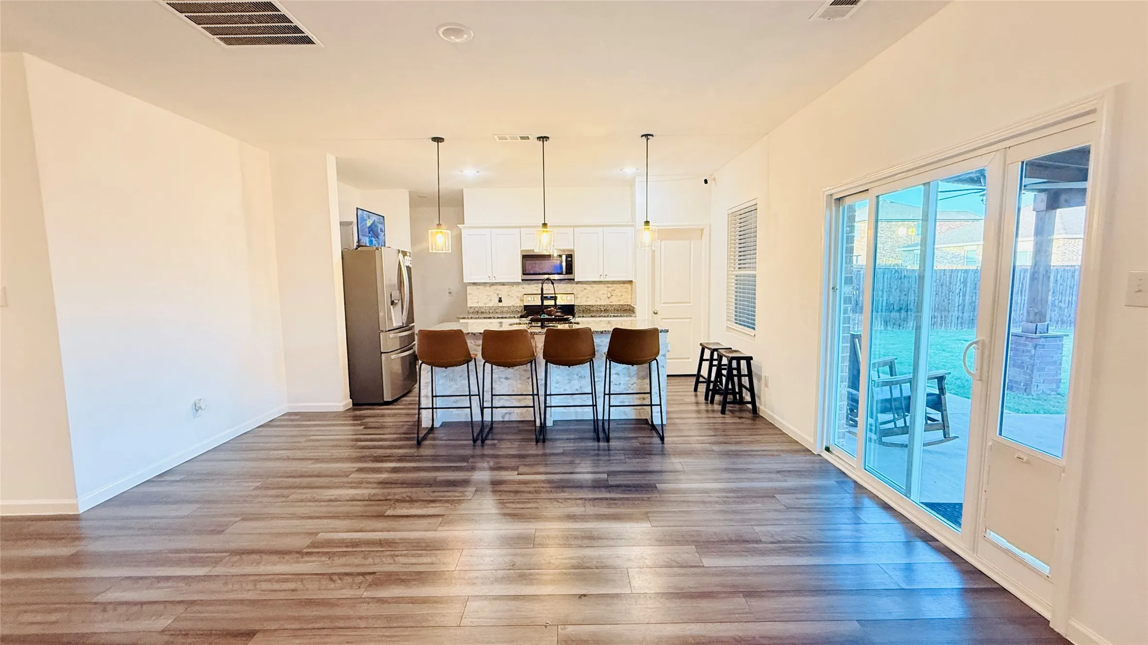 Open-concept living room with laminate-finish flooring, a kitchen island with pendant lighting, stainless steel appliances, and sliding glass doors to the outdoor area