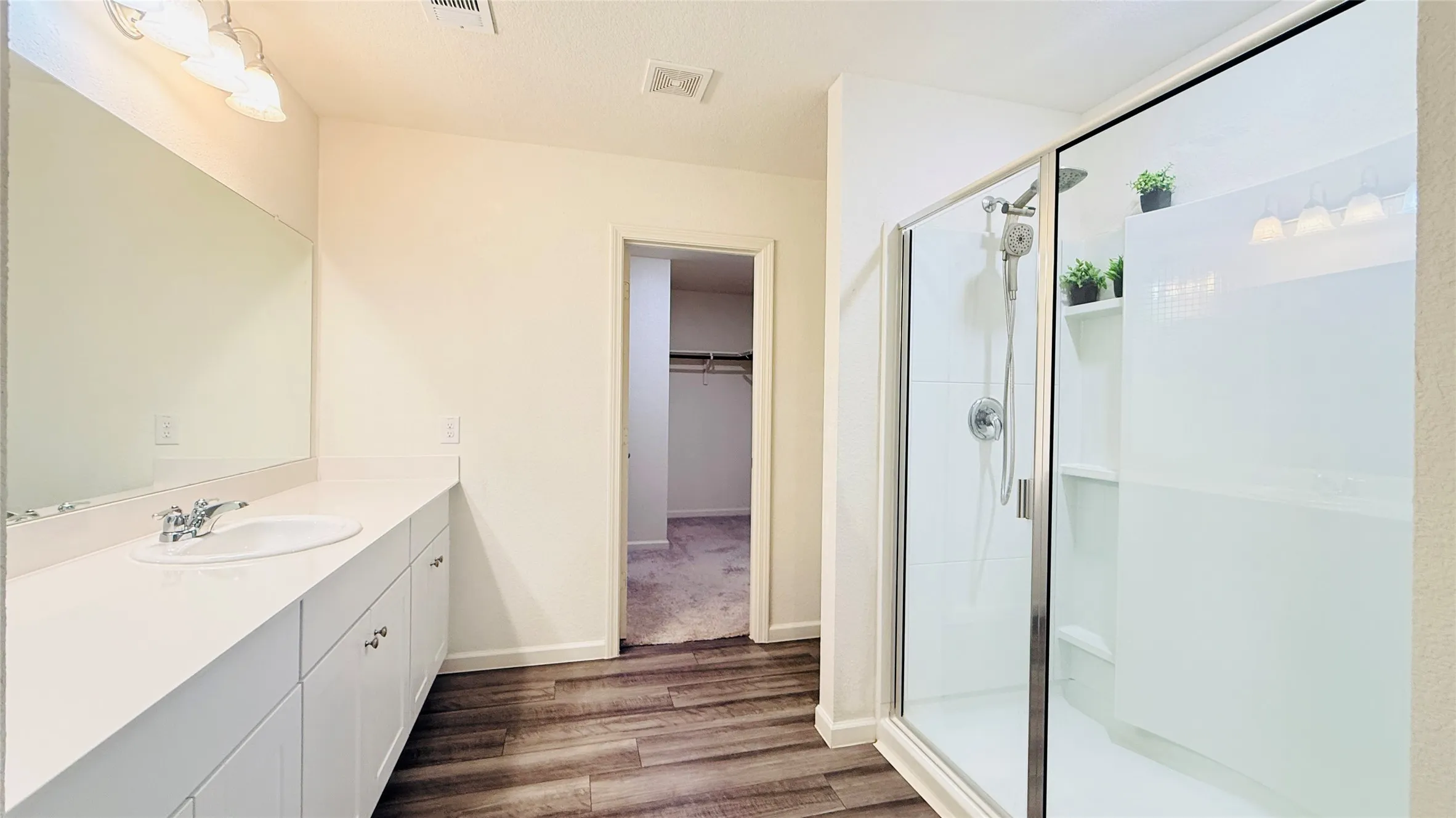 Bathroom featuring a frameless glass shower enclosure with white tiled walls, a white vanity with integrated sink, chrome faucet, and laminate-finish flooring