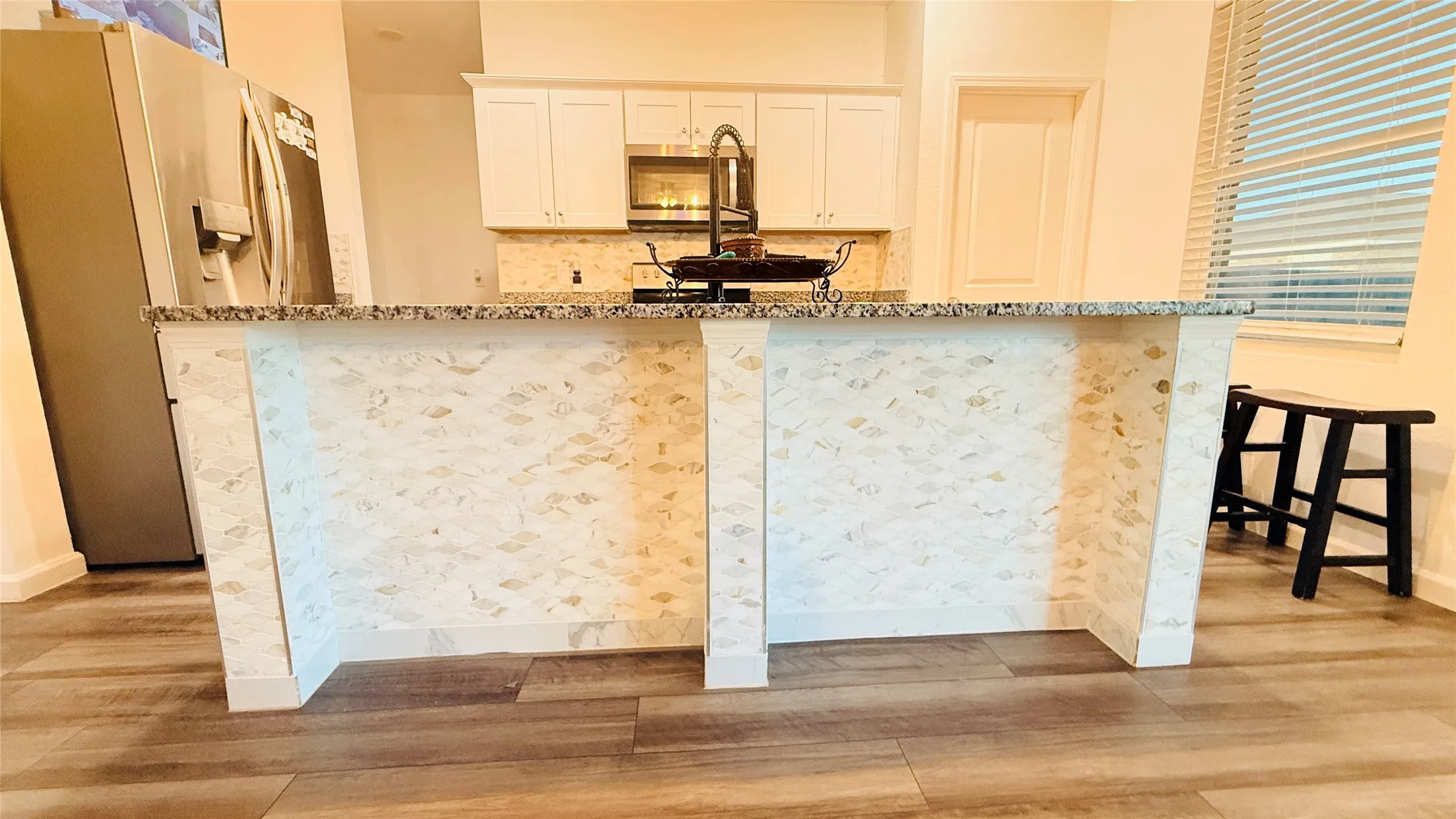 Kitchen island featuring a patterned tile facade, a speckled countertop, and under-counter seating space