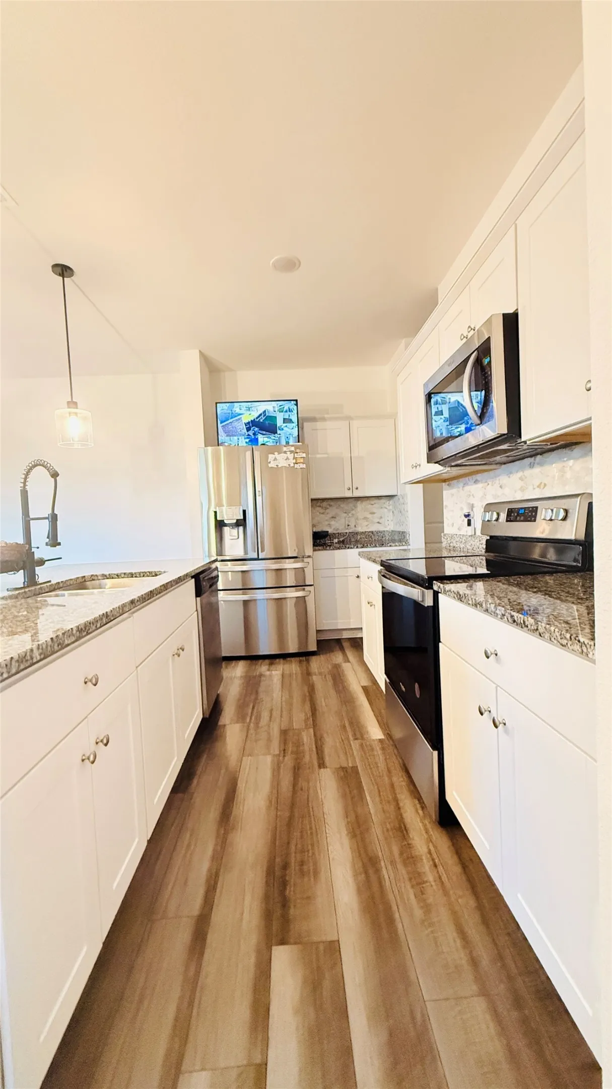 Galley kitchen featuring laminate-finish flooring, white cabinetry with silver hardware, granite-style countertops, and a tiled backsplash