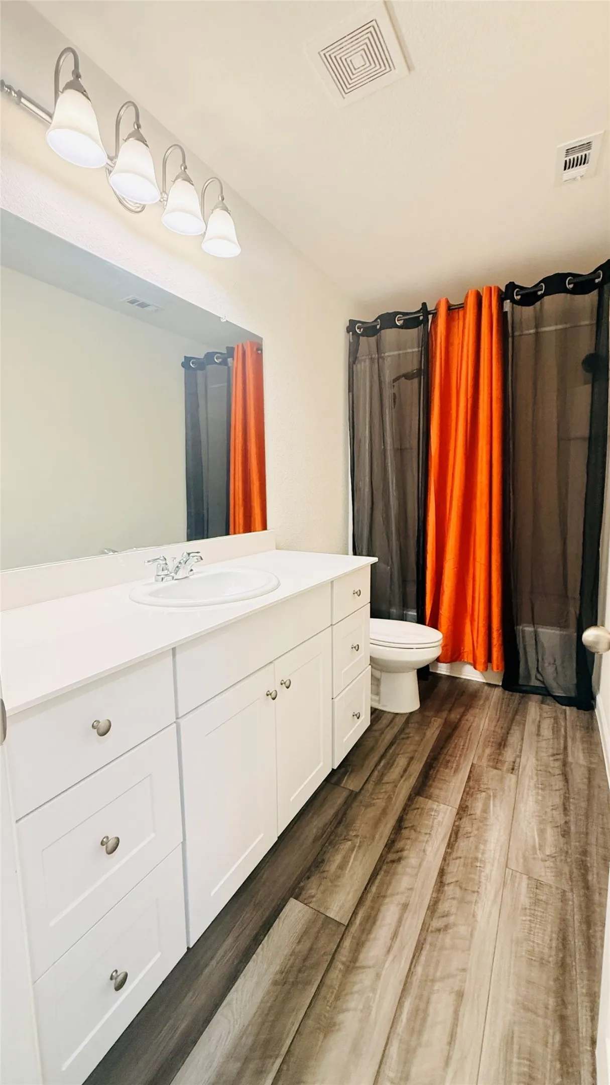 Spacious Second bathroom featuring a white vanity with integrated sink, expansive wall mirror, and laminate finish flooring.