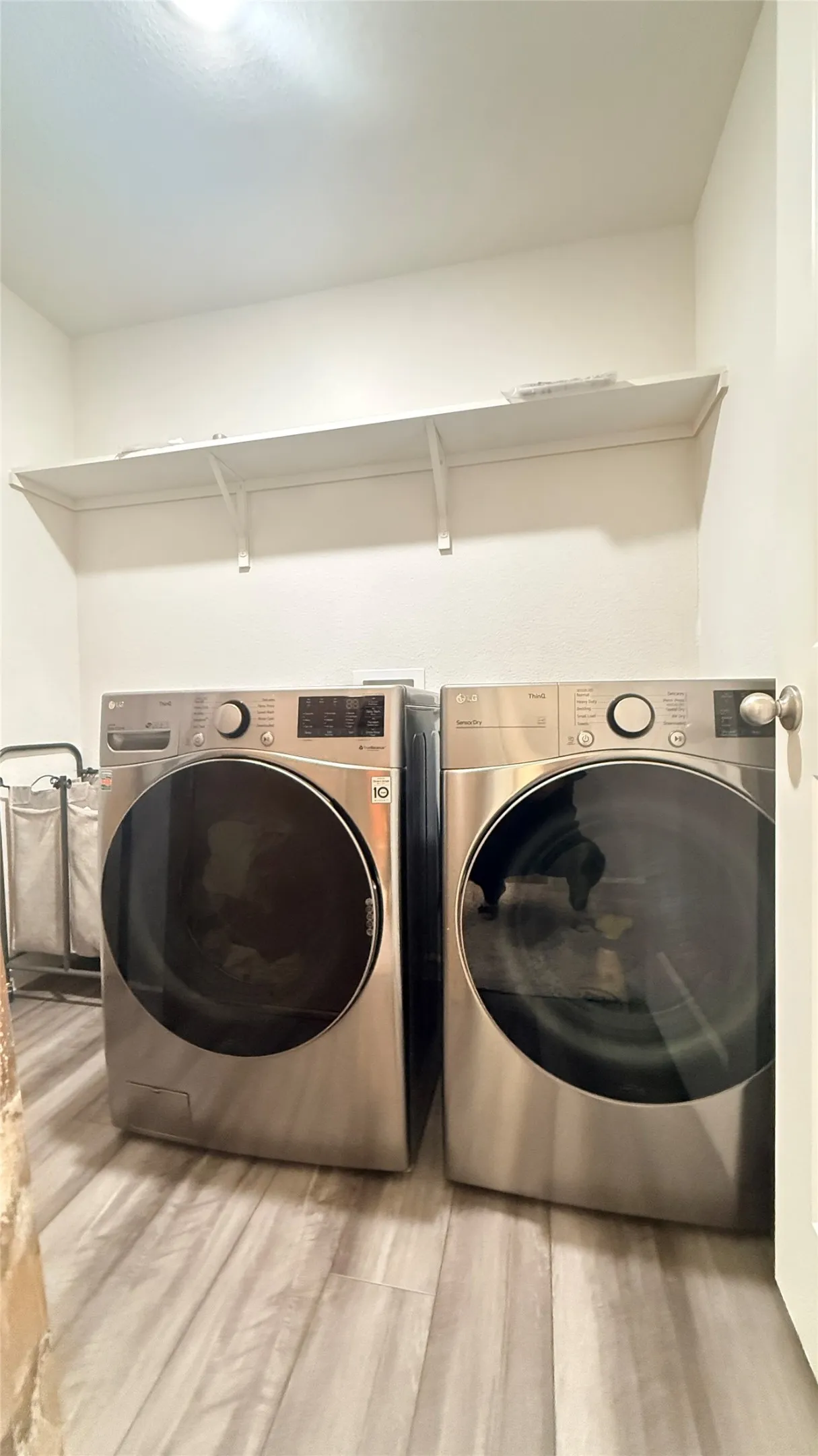 Dedicated laundry area featuring a shelf, light-toned laminate-finish flooring, and white walls