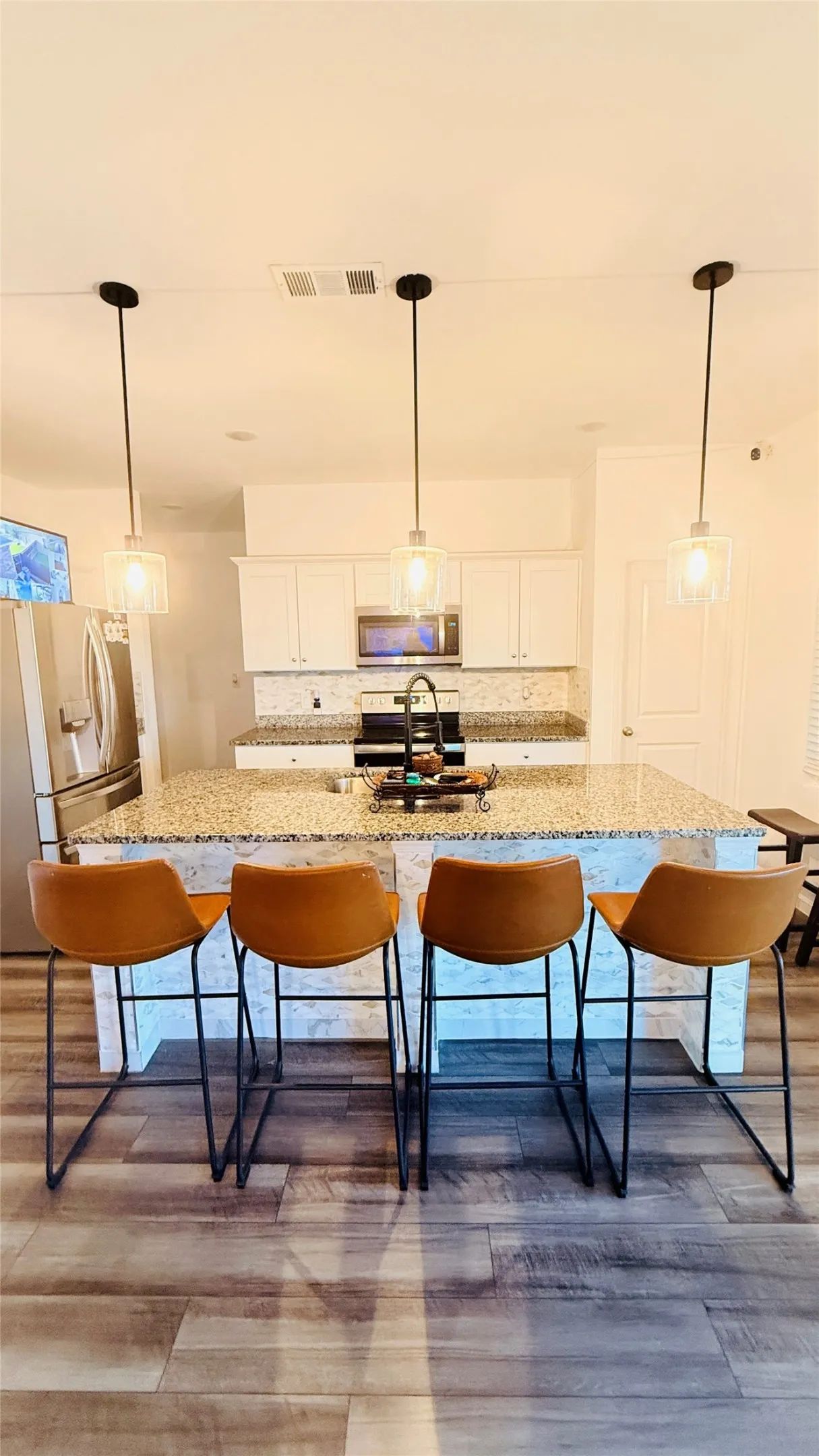 Kitchen island with stone countertop, undermount sink, and three pendant light fixtures