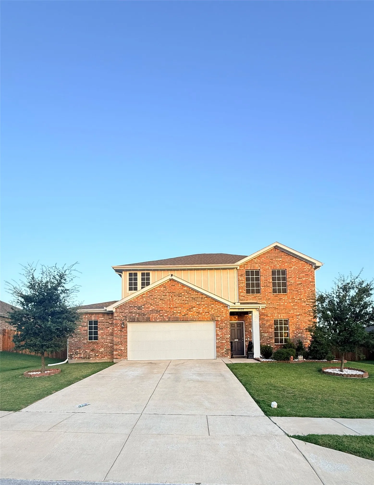 Two-story brick facade residence featuring a two-car garage, a concrete driveway, and a front entry with a covered porch