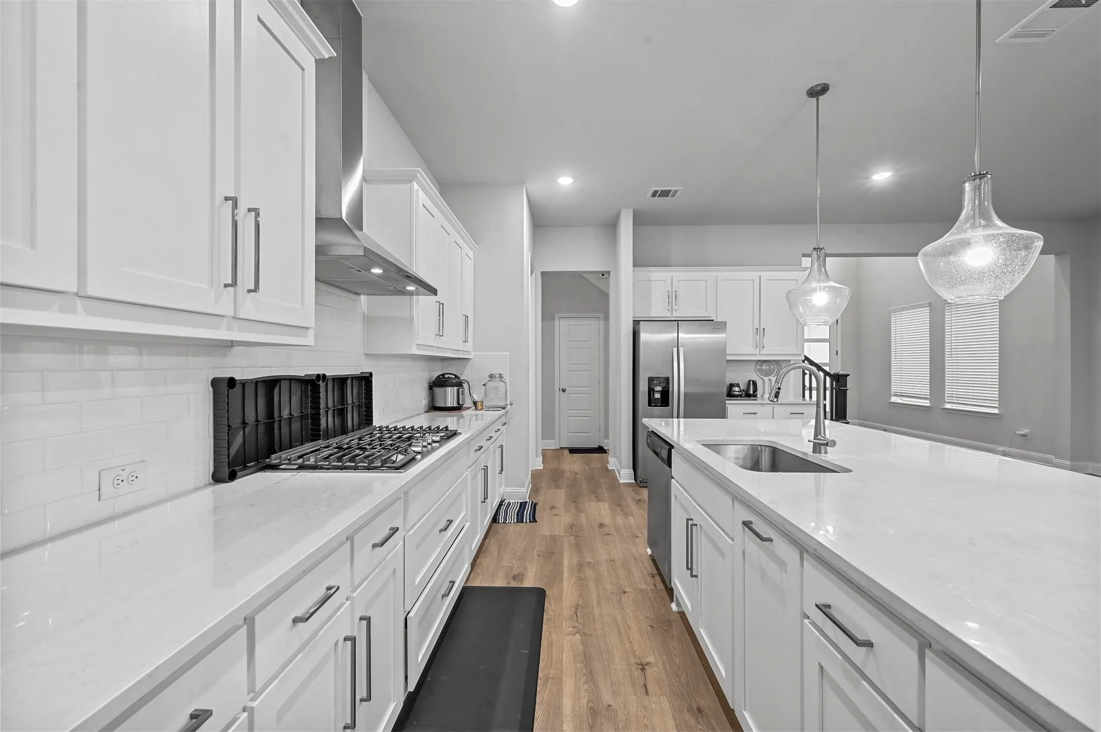Kitchen with white cabinetry, light stone counters, decorative light fixtures, light wood floors, and backsplash