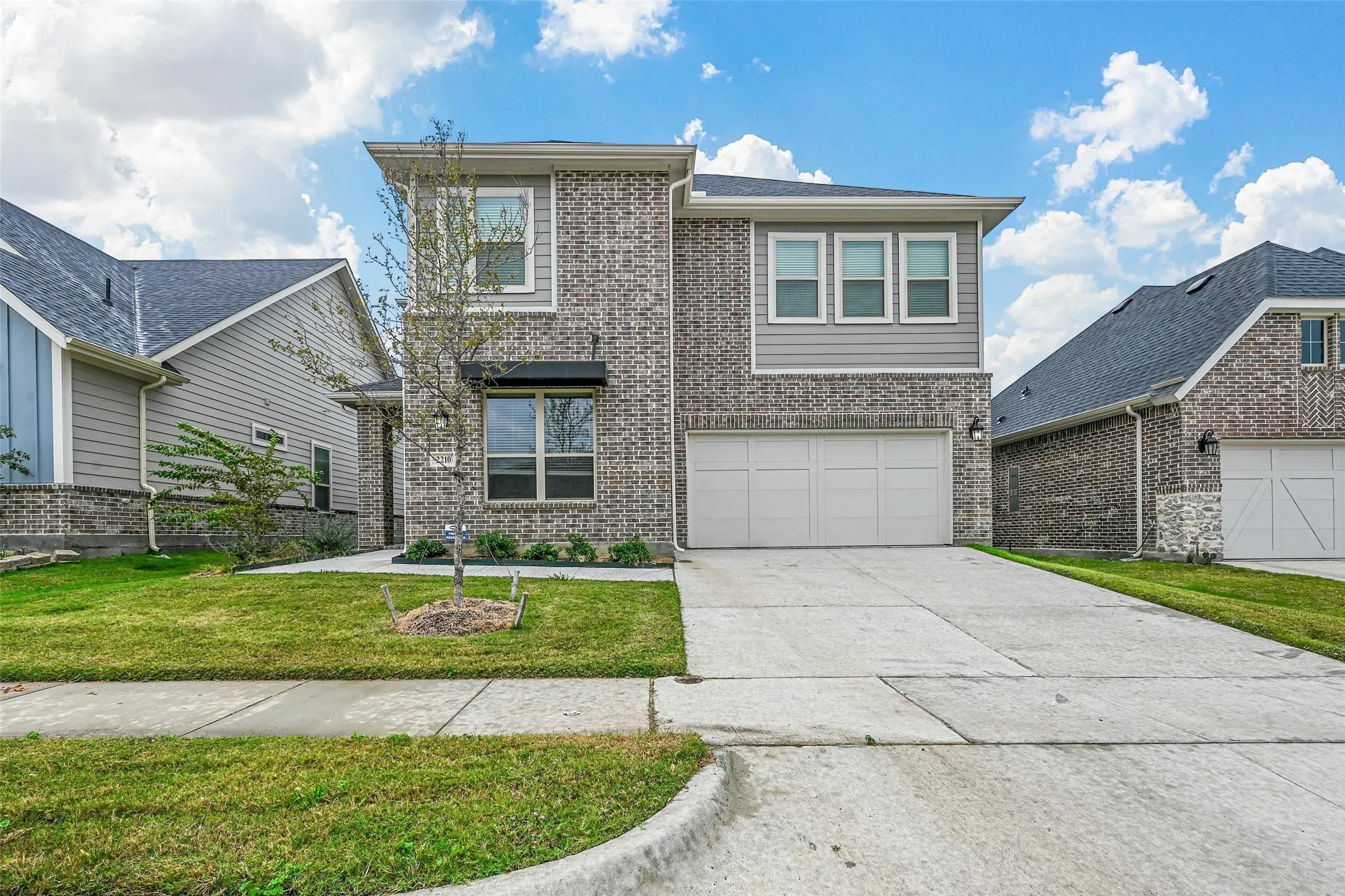 Modern style home featuring a garage, brick siding, driveway, and a front yard
