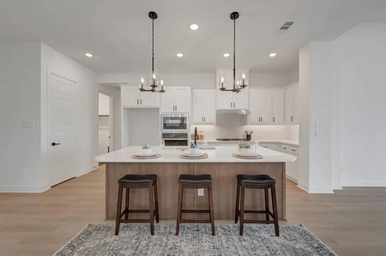 Open-concept kitchen featuring an island with counter seating, white cabinetry, integrated stainless steel appliances, and wood-finish flooring