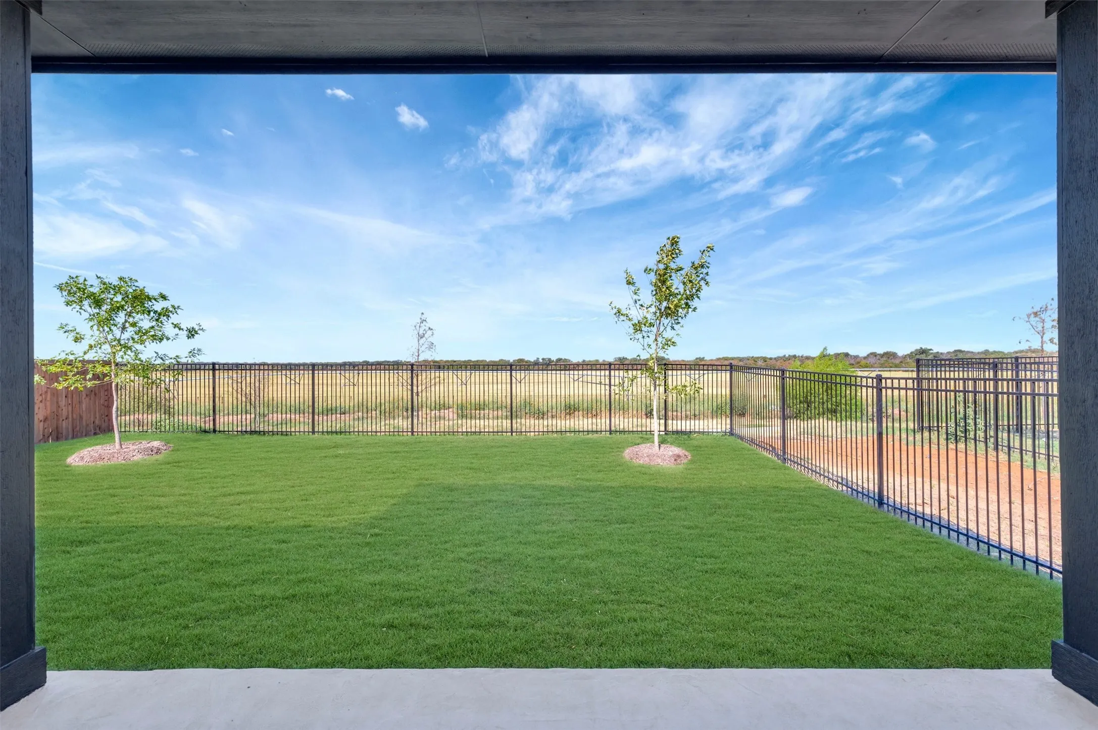Expansive grassy area with a partial privacy fence and a metal perimeter fence
