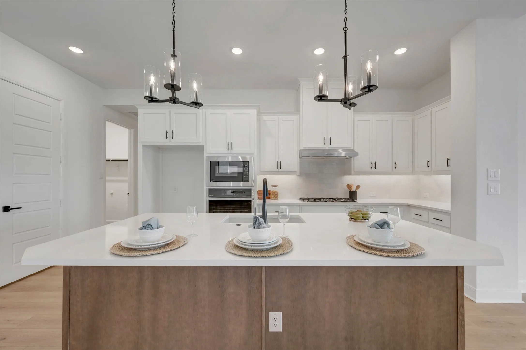 Center island with a white countertop and wood-finish paneling, white cabinetry with dark hardware, built-in stainless steel microwave, and recessed ceiling lighting