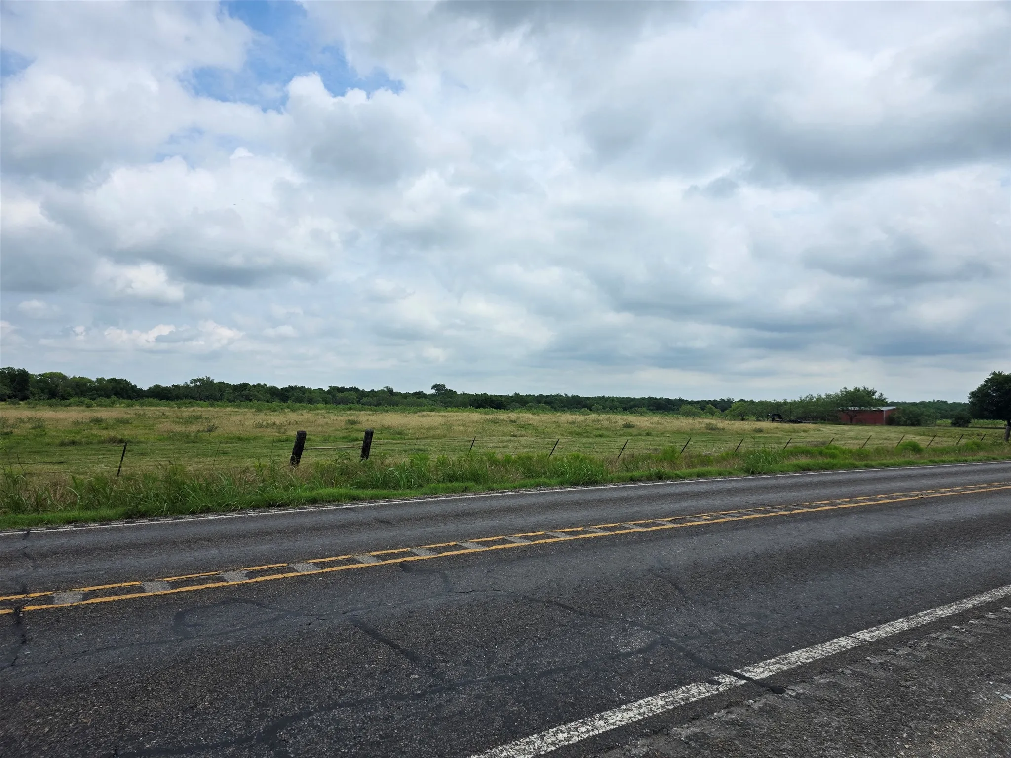Expansive grassy acreage featuring perimeter fencing and a distant red barn structure