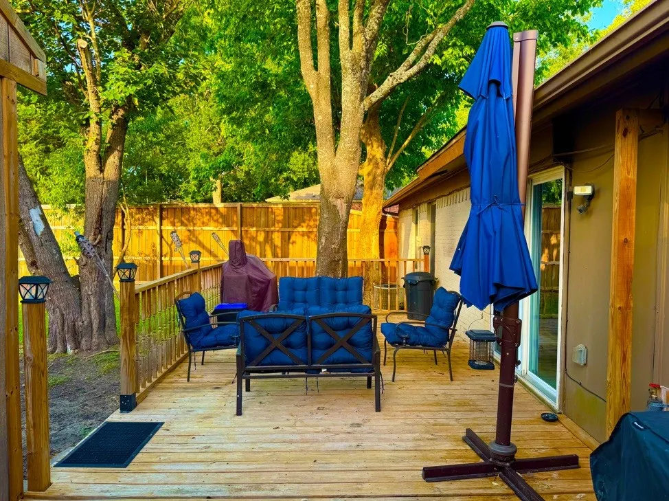 Expansive wood-plank deck featuring a wood railing with post cap lighting, mature trees, a privacy fence, and direct access to the interior via a glass sliding door