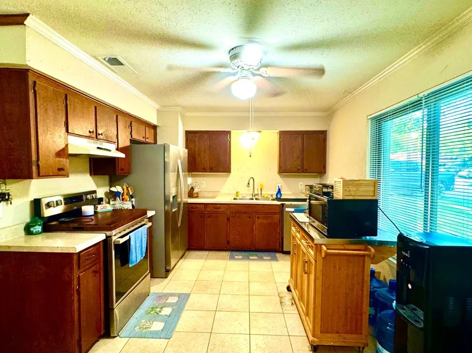 Kitchen featuring wood-finish cabinetry, tile flooring, stainless steel appliances, and a window with horizontal blinds