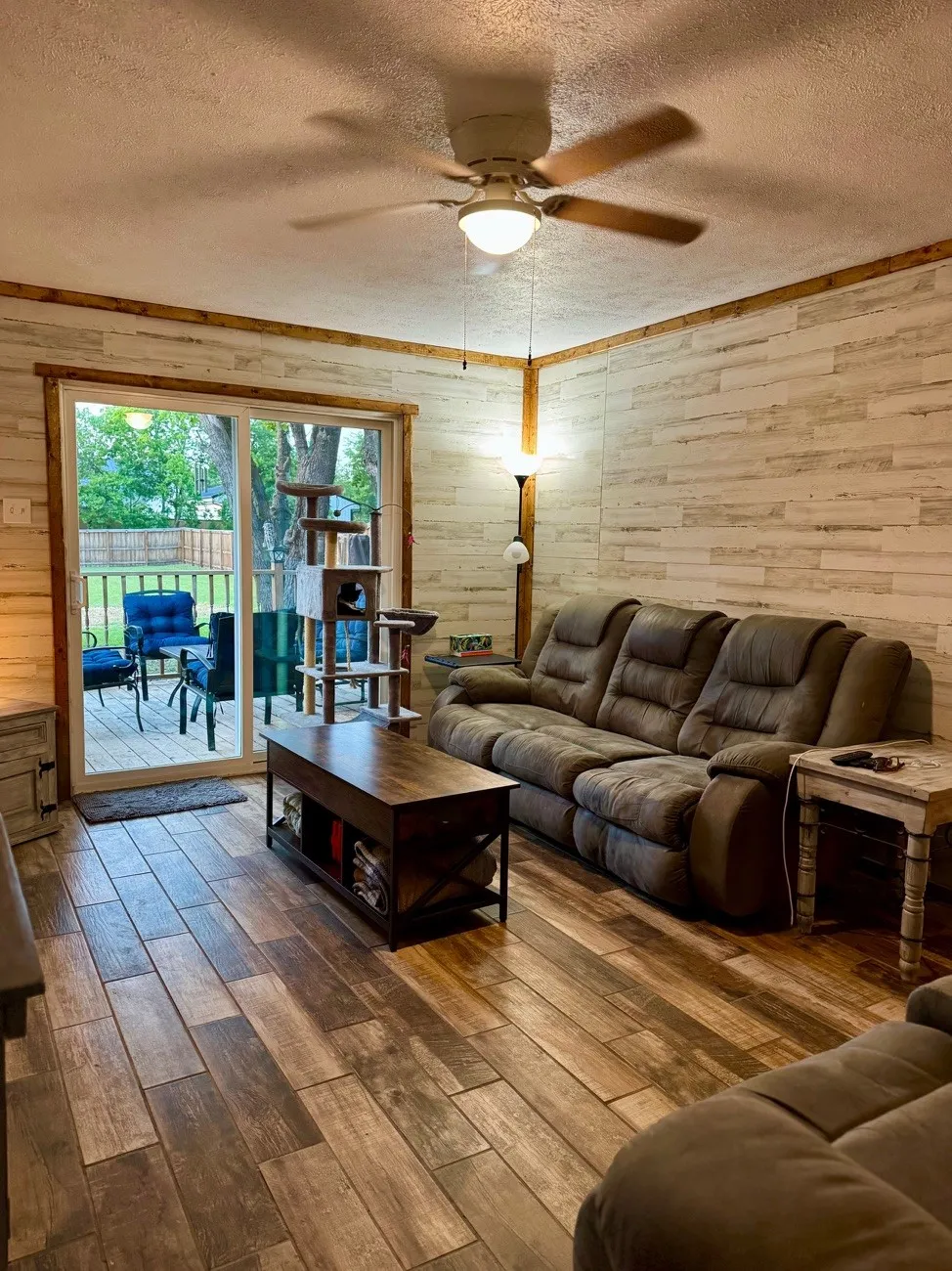 Living area featuring wood-finish flooring, shiplap accent walls, and a ceiling fan with integrated lighting