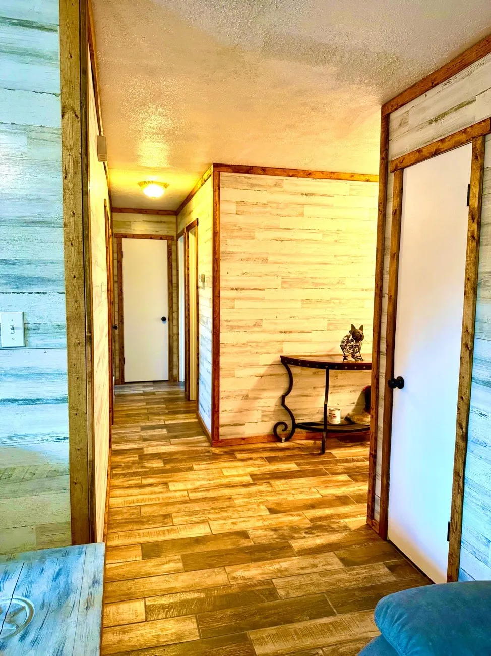 Hallway featuring wood-finish flooring, light-toned horizontal paneling, and contrasting dark wood trim around doorways