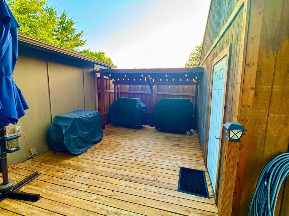 Outdoor deck featuring wood plank flooring and a partially covered grilling station with string lighting
