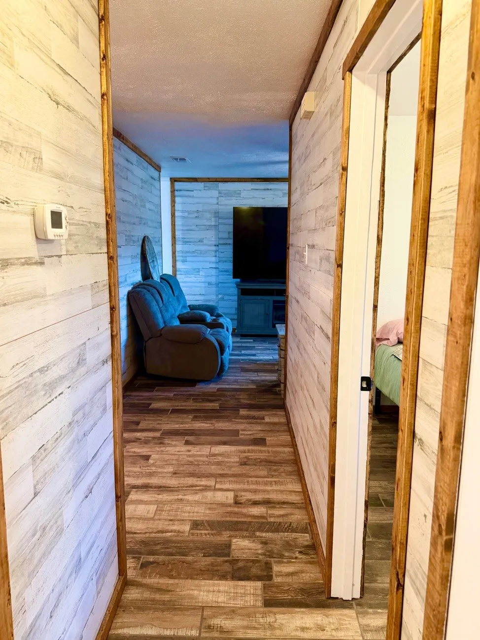 Hallway featuring wood-finish plank tile flooring and shiplap-style wall paneling with natural wood trim