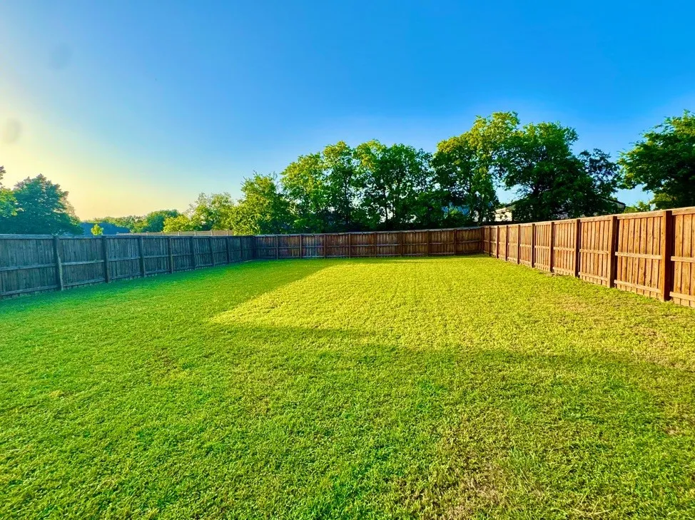 Expansive backyard featuring a lush green lawn, full wood privacy fencing, and surrounding mature trees