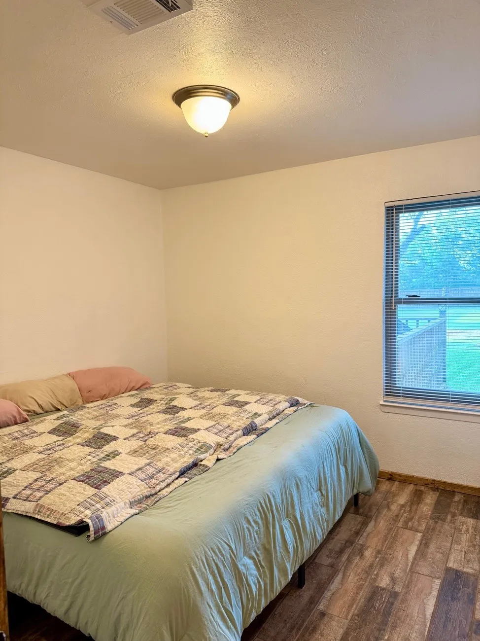 Room featuring wood-finish flooring, a window with horizontal blinds, and a flush-mount ceiling light fixture