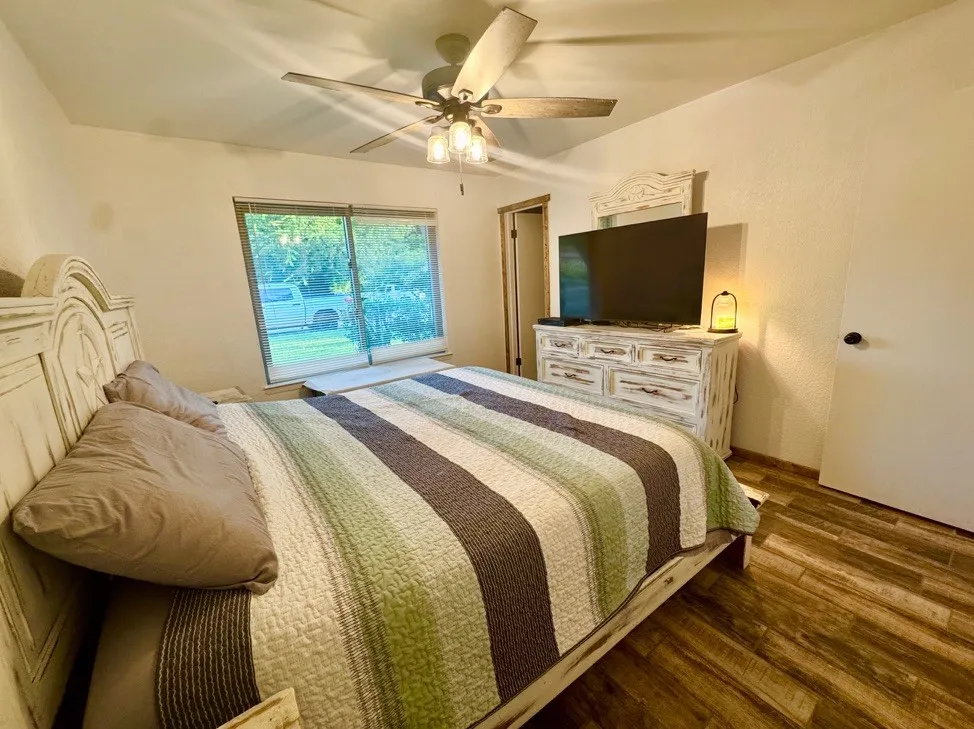Bedroom featuring wood-finish flooring, a ceiling fan with integrated lighting, and a large window